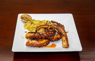 Grilled octopus with smashed potatoes on white square plate on wooden table