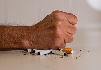 Fist of a man hitting a pile of broken cigarettes on a white table