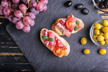 Tasty sandwiches with salami and grapes on dark wooden background