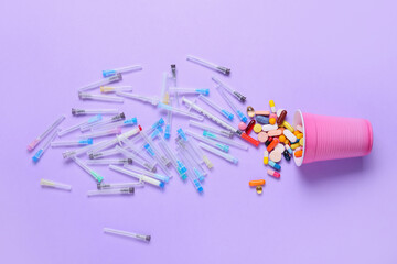 Cup with many pills and syringes on color background