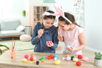 Naklejka premium Cute twin girls painting Easter eggs at home