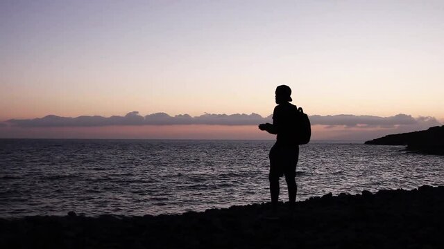 Silhouette of a traveler boy taking a picture at sunset at the beach