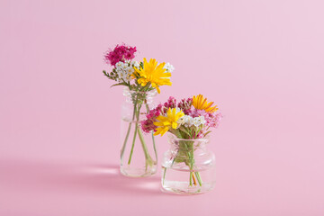 Miniature glass bottles with wildflowers on a pink background