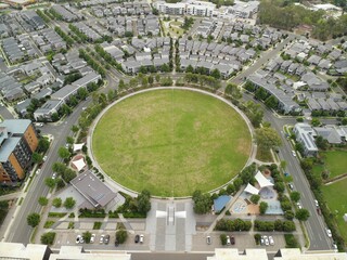 Green grassed cricket oval surrounded by modern housing estate on an overcast day.