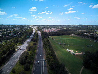 Fototapeta na wymiar Aerial image of the M4 motorway facing east from Glenmore Park, with green sporting fields and suburban homes in the background.