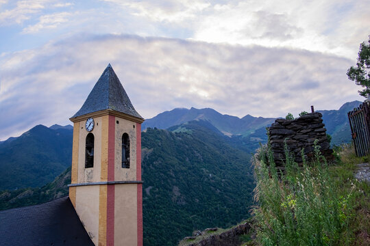 bell tower of the church of the Catalan Pyrenean village of Canejan, with cream, red and yellow colors and the mountains in the background