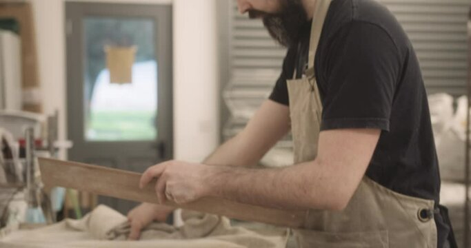 Bearded male baker preparing dough for artisan baguettes working in industrial bakery