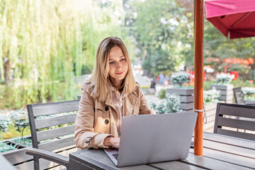 Young Caucasian business woman with blonde hair working on laptop in outdoor cafe. College student using technology , online education, freelance 