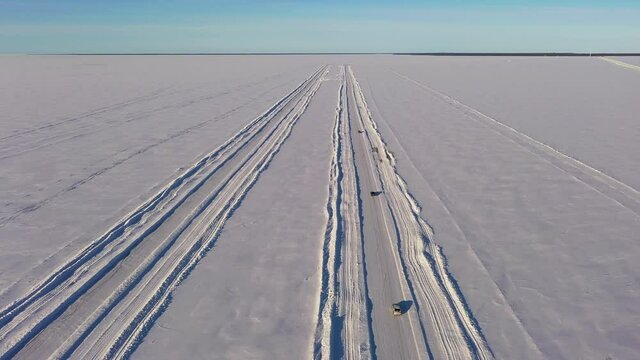 Aerial view of vehicles on a winter road, cars crossing frozen ocean ice - tilt, drone shot