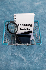 spending habits text on notepad with shopping basket and magnifying glass and payment cards, money and consumer behaviour