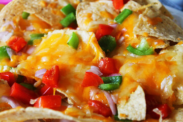Close-up of a plate of nachos, with cheese, onions, and red and green peppers.