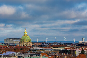 Fototapeta na wymiar Cityscape, amazing view over the city of Copenhagen, Denmark. Winter cloudy picturesque scene with roofs and buildings. Picture taken from Round Tower. Row of wind turbines