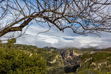 Fototapeta na wymiar Meteora, Greece, Early spring landscape of the cliffs, monastery and cloudy sky. Leafless tree branch in the foreground