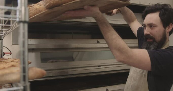 Portrait of bearded male baker taking fresh sourdough bread out of the oven