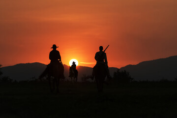 Vintage and silhouettes of a group of cowboys sitting on horseback at sunset.