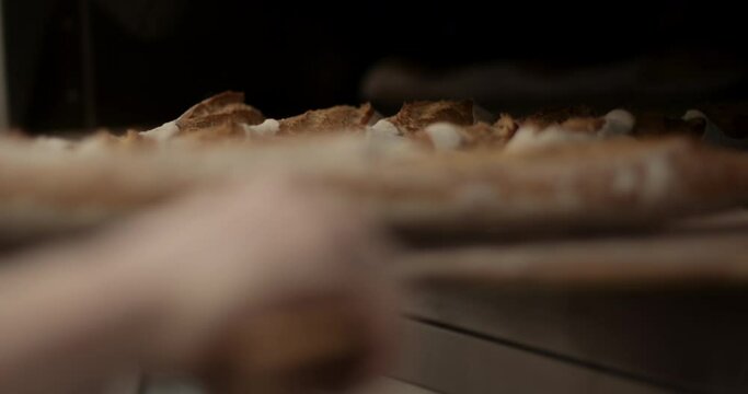 Close up of male baker taking freshly baked baguettes out of oven in bakery