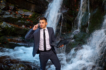 Business man in suit with laptop at waterfall background. Waterproof device concept. Telework businessman.