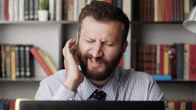 Earache, ear pain, itchy. Handsome man at workplace touches his ear with finger experiencing pain and itchy. Slow motion