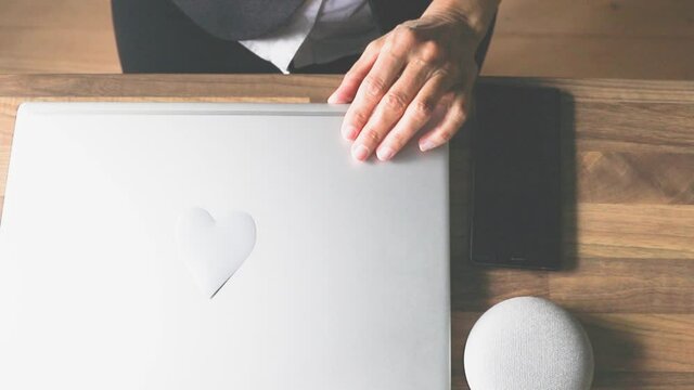 Eine Frau im B&uuml;ro oder Homeoffice klappt den Laptop zu, auf dem ein Herz geklebt ist. Mit Liebe zum Beruf und mit viel Motivation. 