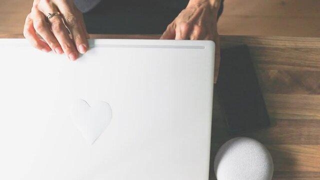 Eine Frau im B&uuml;ro oder Homeoffice klappt den Laptop zu, auf dem ein Herz geklebt ist. Mit Liebe zum Beruf und mit viel Motivation. 