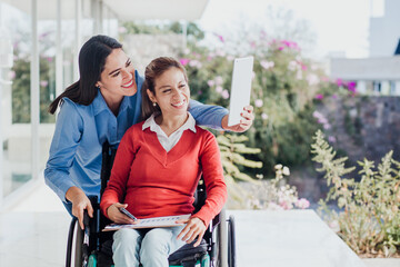 hispanic woman in wheelchair taking a selfie photo at workplace with another woman in Mexico
