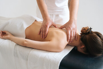 Obraz na płótnie Canvas Male masseur massaging back and shoulder blades of young woman lying on massage table on white background. Concept of massage spa treatments.