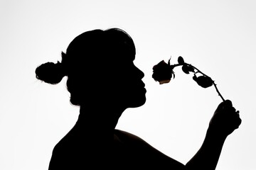 A studio photo  of a silhouetted woman smelling a rose.