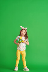 charming happy girl with Easter bunny ears and a bouquet of spring tulip flowers made of fabric on a green background in full growth. the child smiles and rejoices at the arrival of spring and Easter.