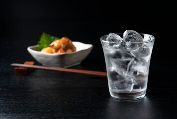 Shochu and nibbles set against a black wood grain background.