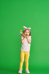 charming happy girl with Easter bunny ears and a bouquet of spring tulip flowers made of fabric on a green background in full growth. the child smiles and rejoices at the arrival of spring and Easter.