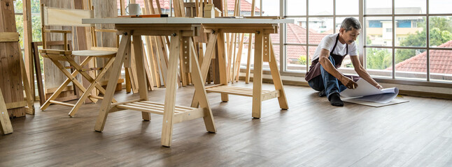 Aged Asian joiner working with blueprint on floor - Powered by Adobe