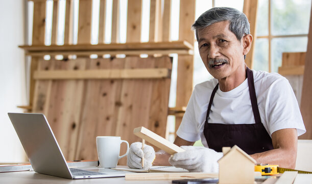 Senior Asian carpenter writing down data from laptop