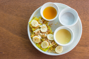 The Roti with sliced banana was served with sweetened condensed milk sugar and banana sauce , on top with sliced almond  put on white plate.