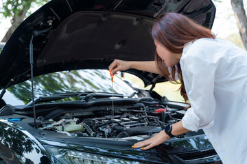 Young asian businesswoman checks the car's engine oil by herself.