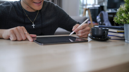 Obraz premium Cropped shot of happy young man freelancer holding stylus pen writing on screen of digital tablet.