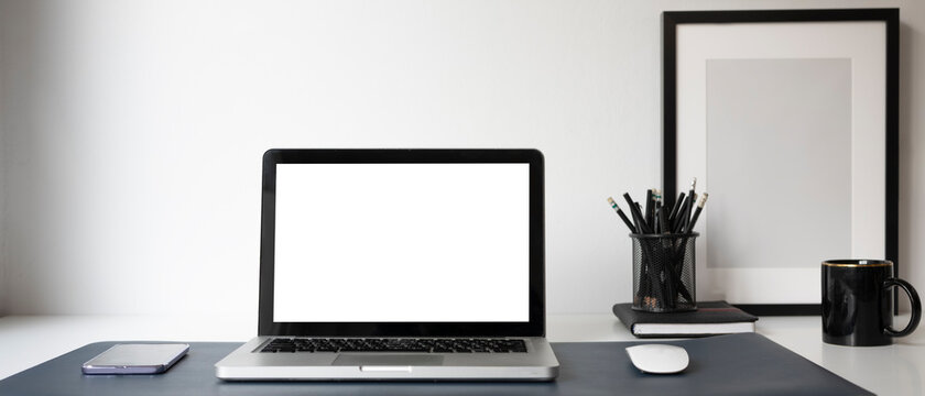 Horizontal image of mock up computer laptop with white screen, smart phone, coffee cup and stationery at modern workplace.