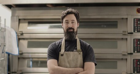 Portrait of bearded male baker in bakery with oven wearing apron - Powered by Adobe