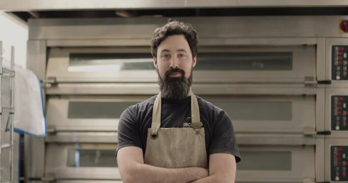 Portrait of bearded male baker in bakery with oven wearing apron