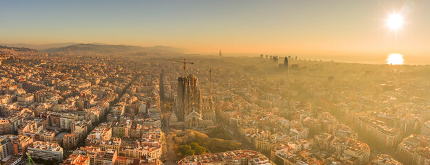 Aerial panorama drone shot of Barcelona skyline with sunrise over horizon in foggy golden hour morning in Spain winter