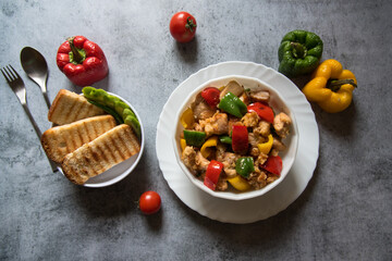 Chicken and bell peppers stir fried in a bowl along with bread slices on a background