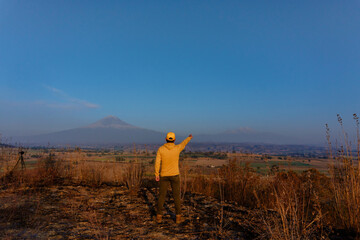 Back view of a young male wearing a yellow hoodie and cap pointing to the mountains