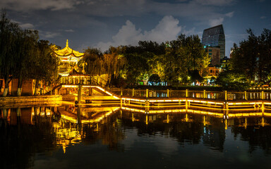 Green lake park scenic view at night with illuminated path and pavilion over a pond Kunming Yunnan China