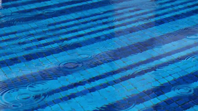 4k Tilting Footage Of Heavy Rain Falling On An Outside Blue Tiled Swimming Pool