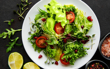 Fresh green mixed  salad bowl with tomatoes and microgreens  on black concrete background. Healthy food, top view.