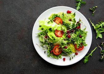 Fresh green mixed  salad bowl with tomatoes and microgreens  on black concrete background. Healthy food, top view.