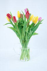 A bouquet of flowers on a white background. Multicolored tulips stand in a transparent jug. Festive mood. There is room for text
