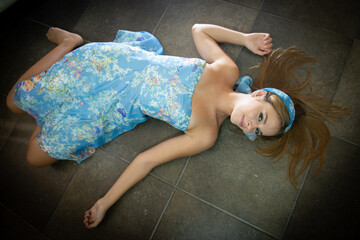 A girl 16 y old is wearing a light blue dress and laying on the ground with spread arms. 