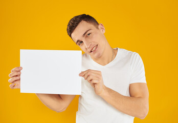 The guy with a sheet of paper on a yellow background tilted his head to the side cropped view