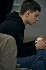 Staged photo illustrates problems and conflicts in gay couple relationships. Moment of showdown: upset black-haired man is sitting near his partner and holding white cup. 