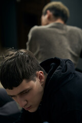 Staged photo illustrates problems and conflicts in gay couple relationships. Moment of showdown: upset black-haired man faced away from his partner in gray cardigan. 